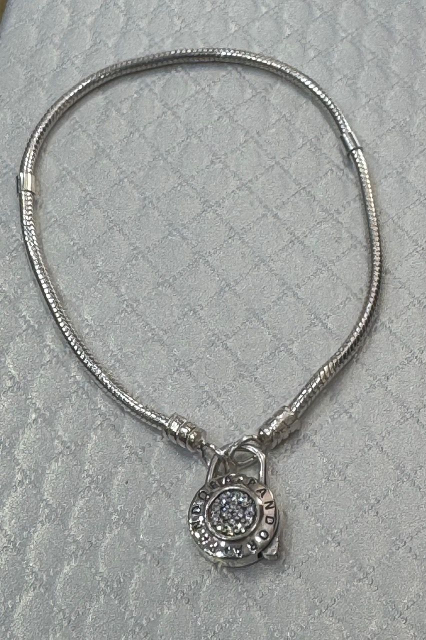 Collar de plata con colgante redondo adornado con diamantes sobre una superficie blanca texturizada.