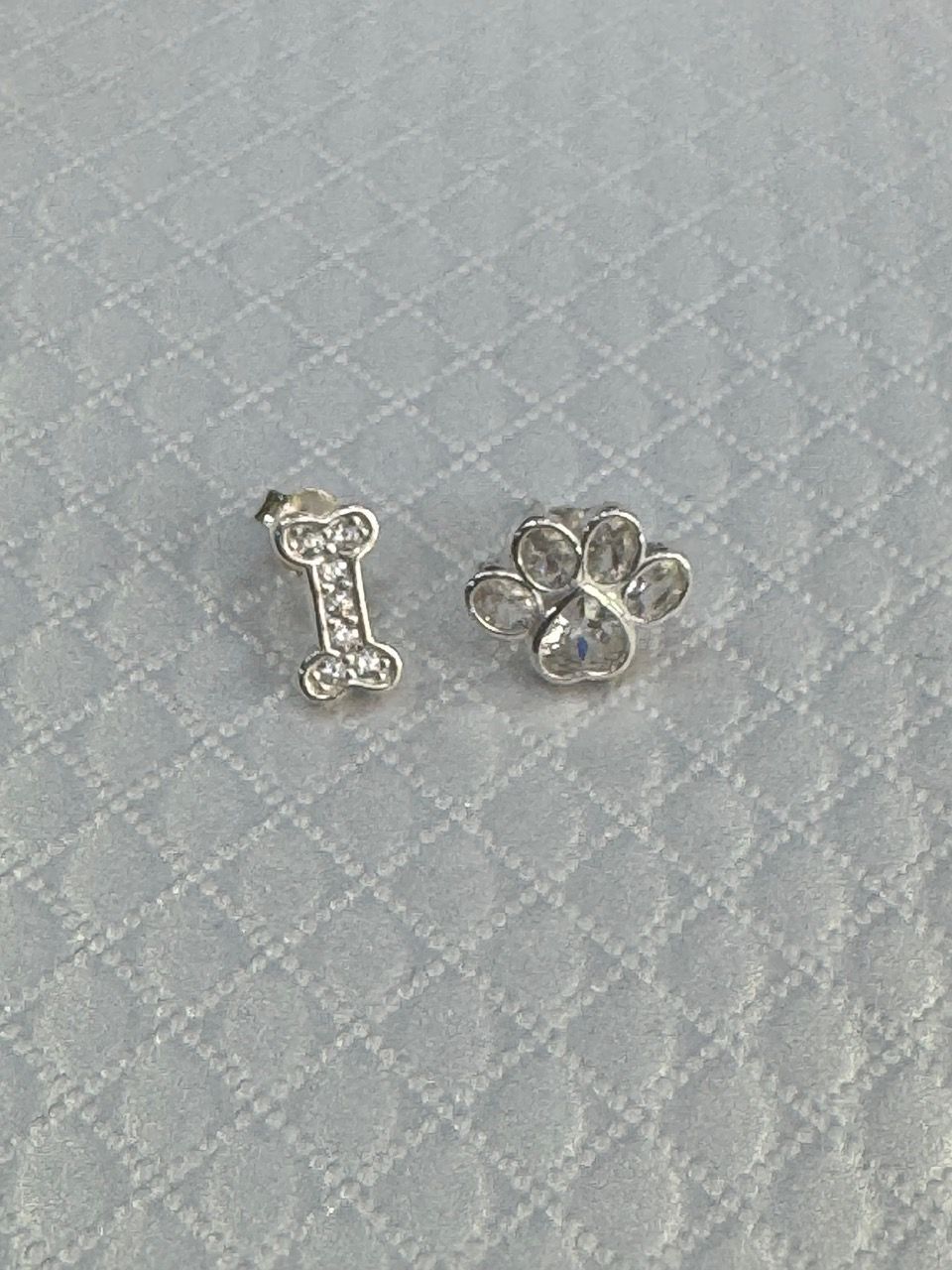 Pendientes de plata con cristales transparentes sobre una superficie texturizada blanca.