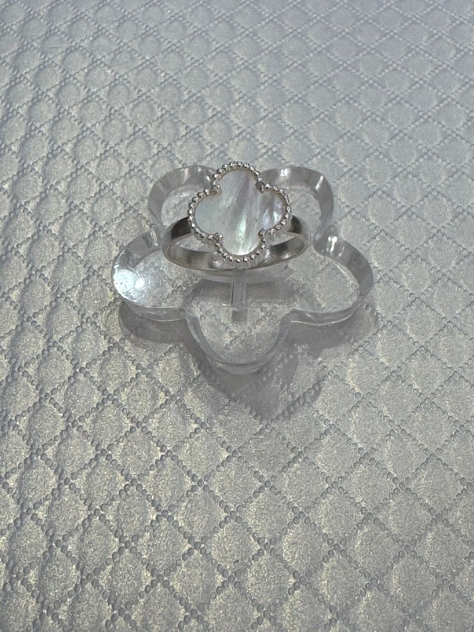 Anillo de trébol de plata con centro de nácar y detalles de diamantes sobre una superficie acolchada.