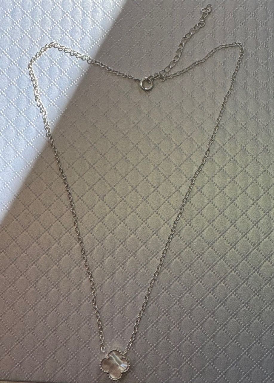 Collar de plata con colgante de trébol sobre una superficie blanca texturizada.