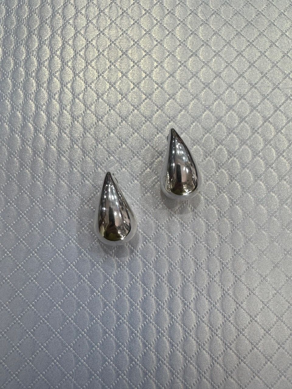 Pendientes de plata en forma de lágrima sobre una superficie de plata texturizada.