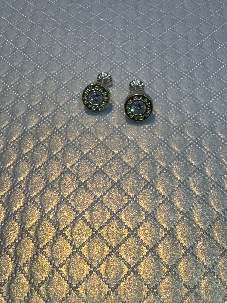 Pendientes de plata con piedras transparentes sobre una superficie con diseño de diamantes.