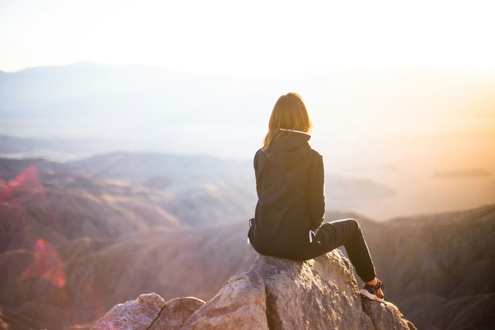 A woman is sitting on top of a rock looking at the mountains.