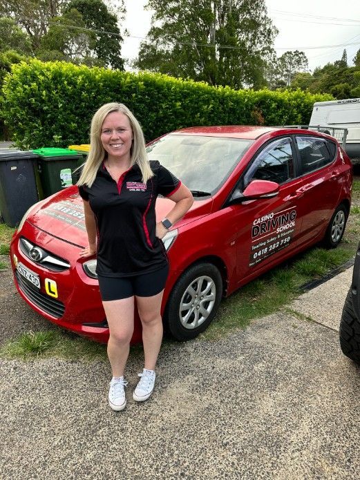 A Woman is Standing in Front of a Red Car — Casino Driving School In Evans Head, NSW