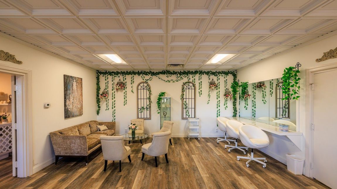 Salon interior with floral accents, mirrors, seating, and styling stations under a textured ceiling.