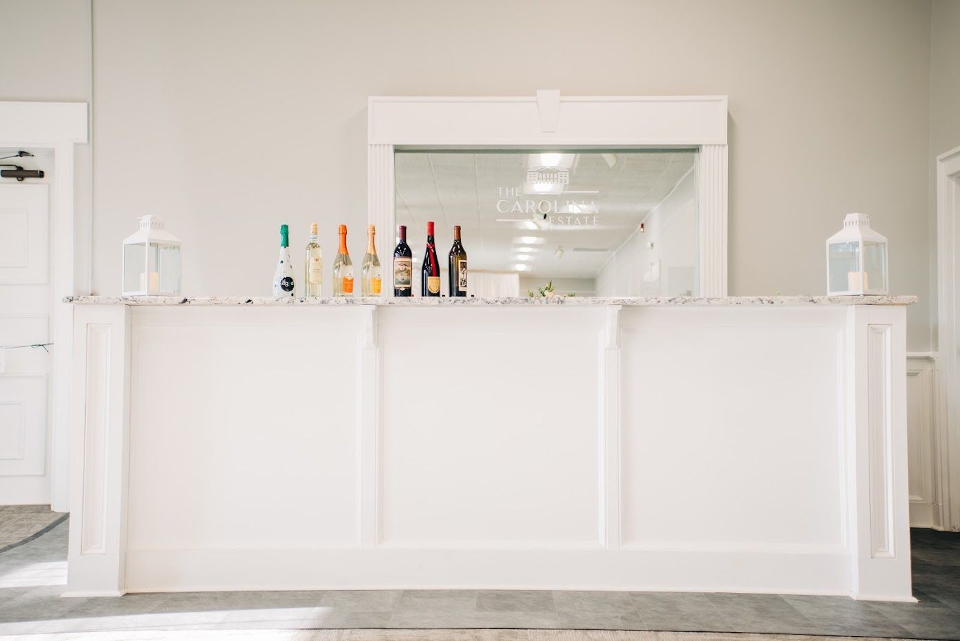 White bar with a granite countertop and bottles of liquor, with a mirror in the background.