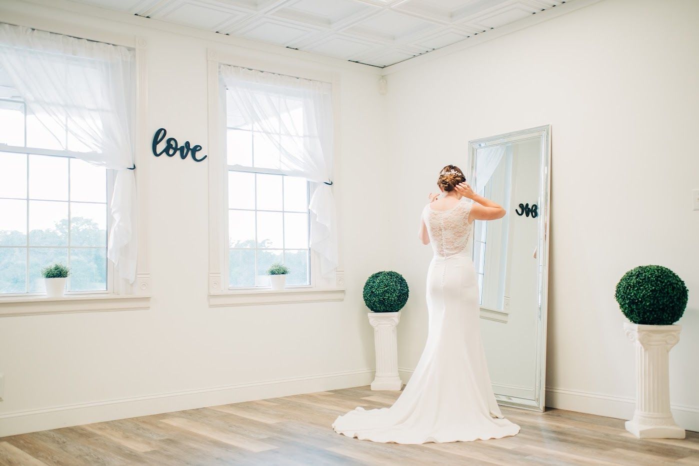 Bride in wedding dress looks at herself in a full-length mirror, light and airy room.