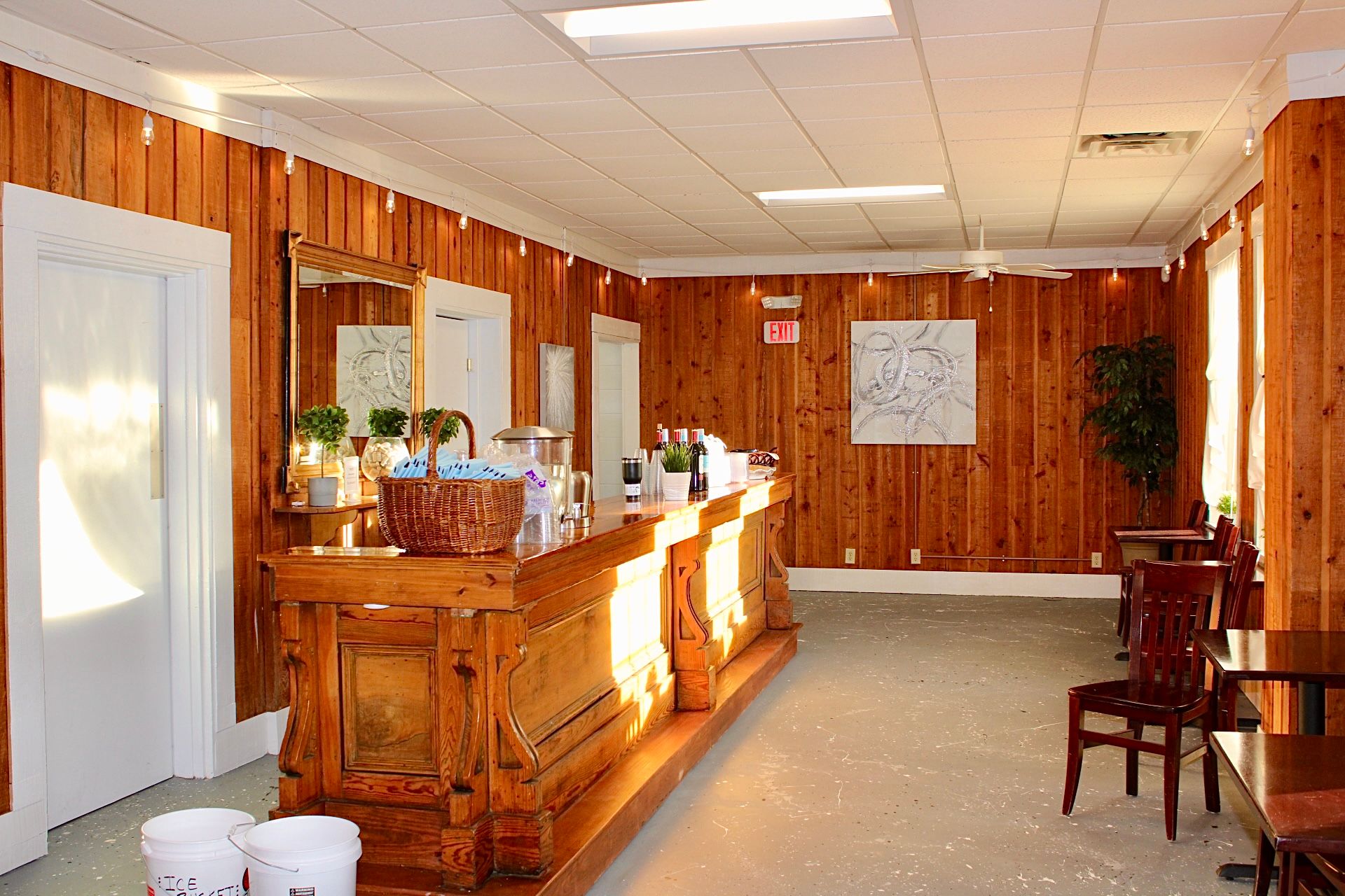Wooden bar in a room with wood paneling, white ceiling, and a few tables and chairs.