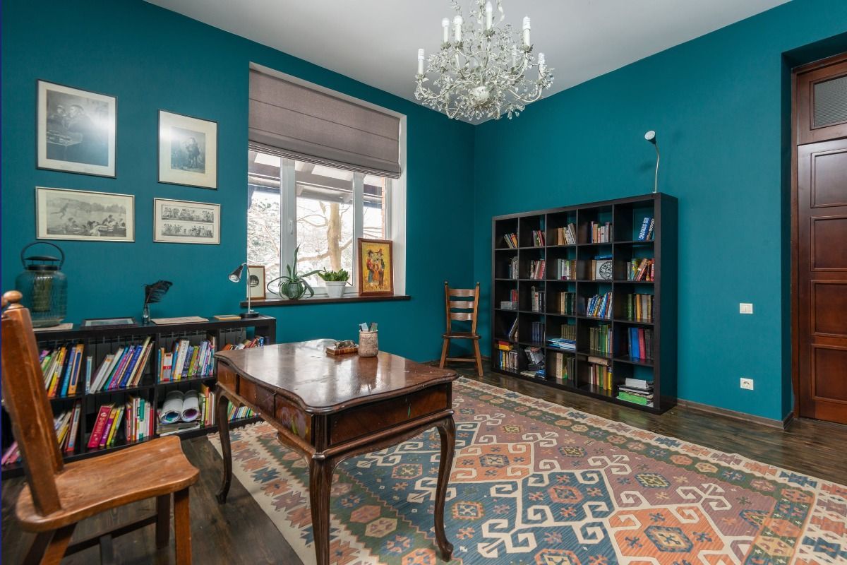 A living room with blue walls , a wooden table , chairs , bookshelves and a chandelier.