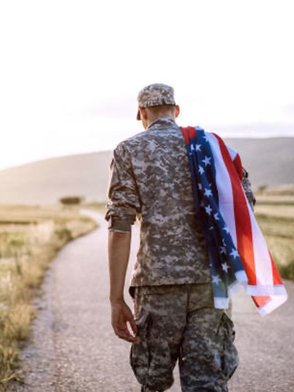 a man in a military uniform, walking down a road with a flag draped over his shoulder