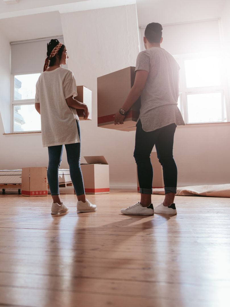 man and woman carrying moving boxes in a home