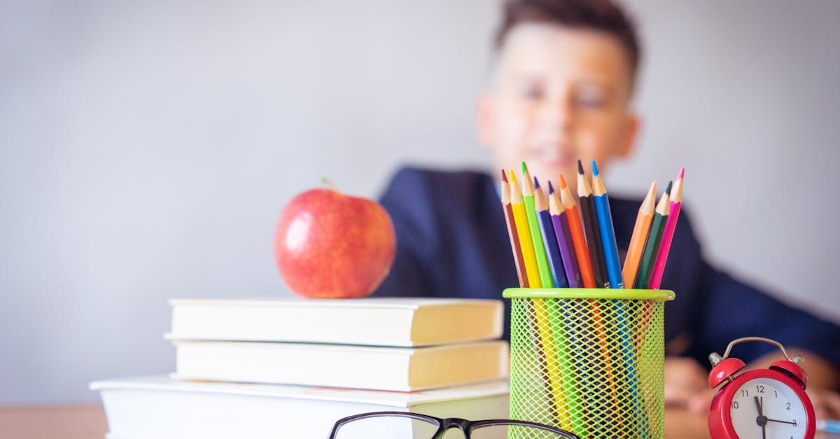 Books, pencils and an apple on a desk with a young boy blurred in the background