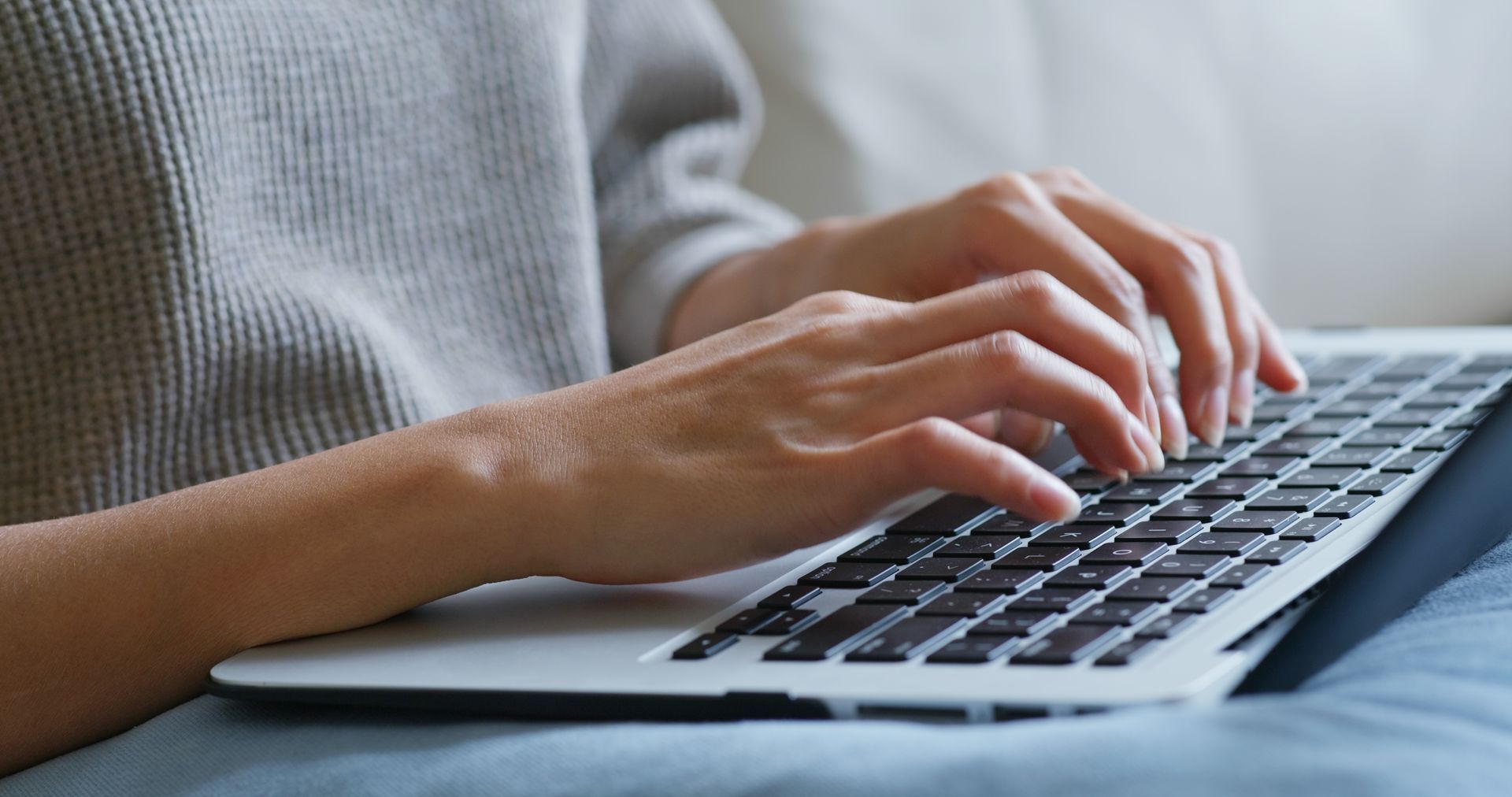 Hands typing on a laptop keyboard while sitting on a couch.