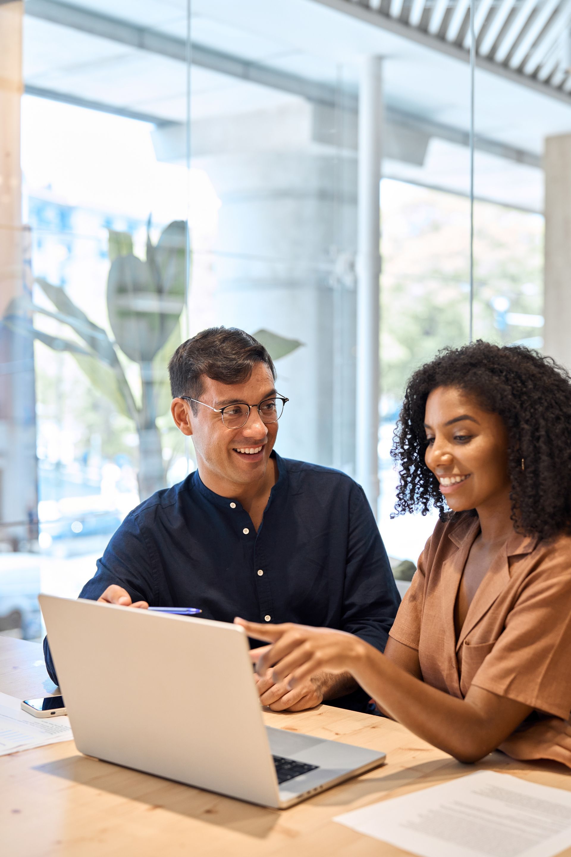 Two colleagues smiling and discussing work at a laptop in a bright office