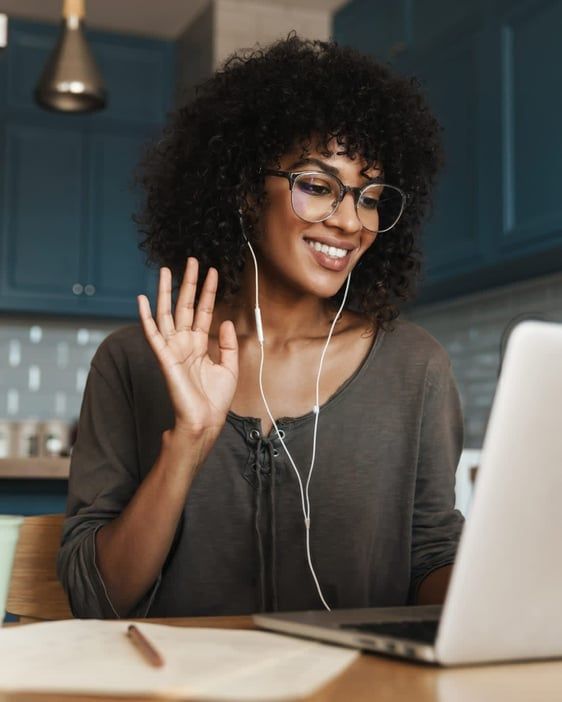 Smiling woman waves on a laptop video call in a kitchen