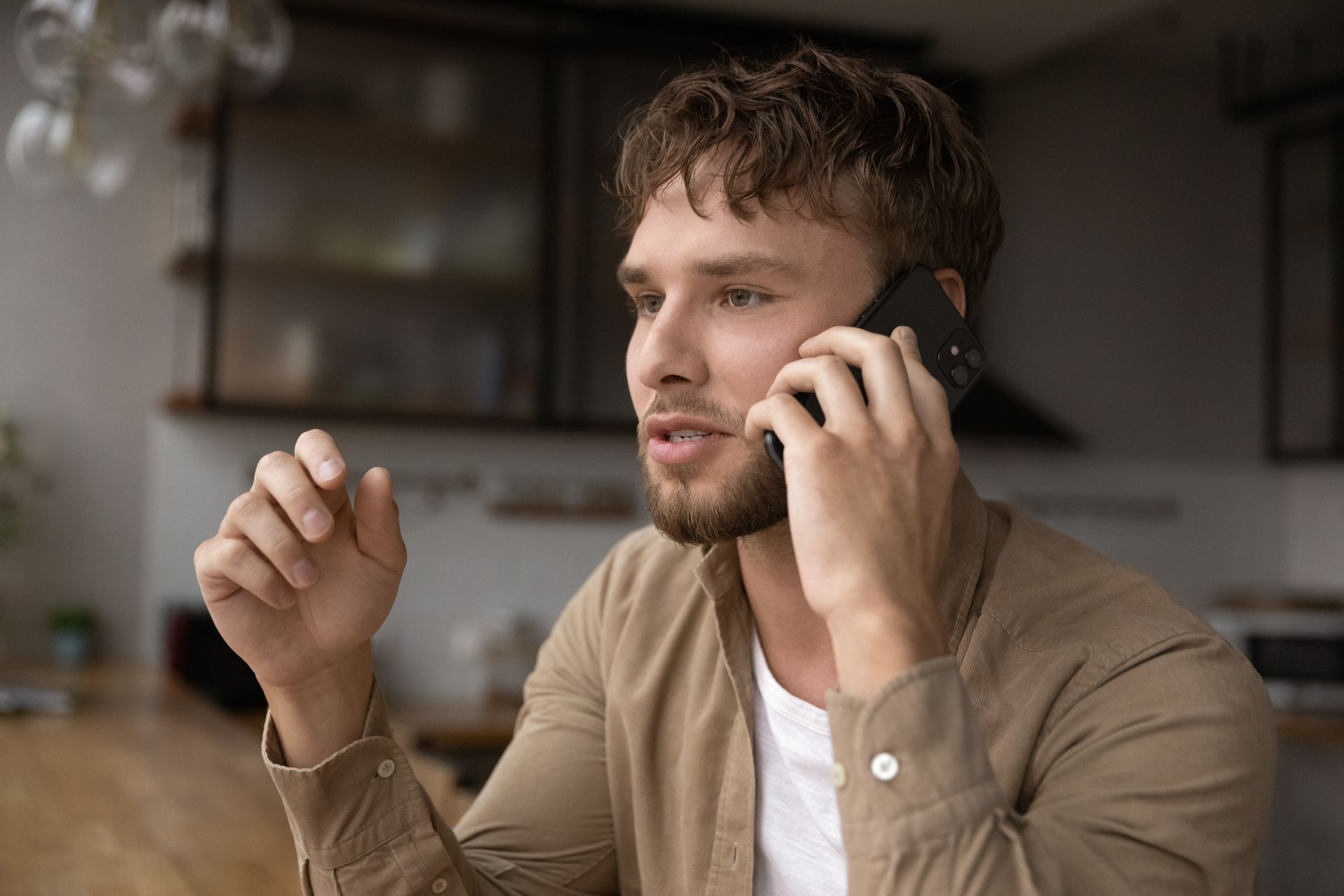 Man sitting indoors, holding a phone to his ear and gesturing with the other hand.