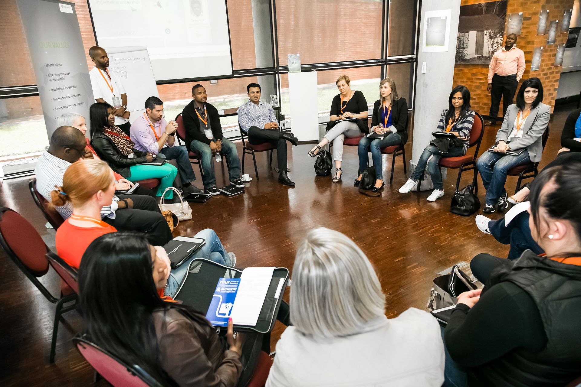 Small group in a bright room sitting in a circle, one woman speaking during a discussion.