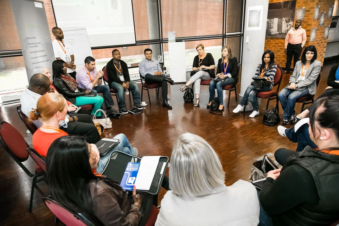 People seated in a circle in a bright room, participating in a discussion or workshop.