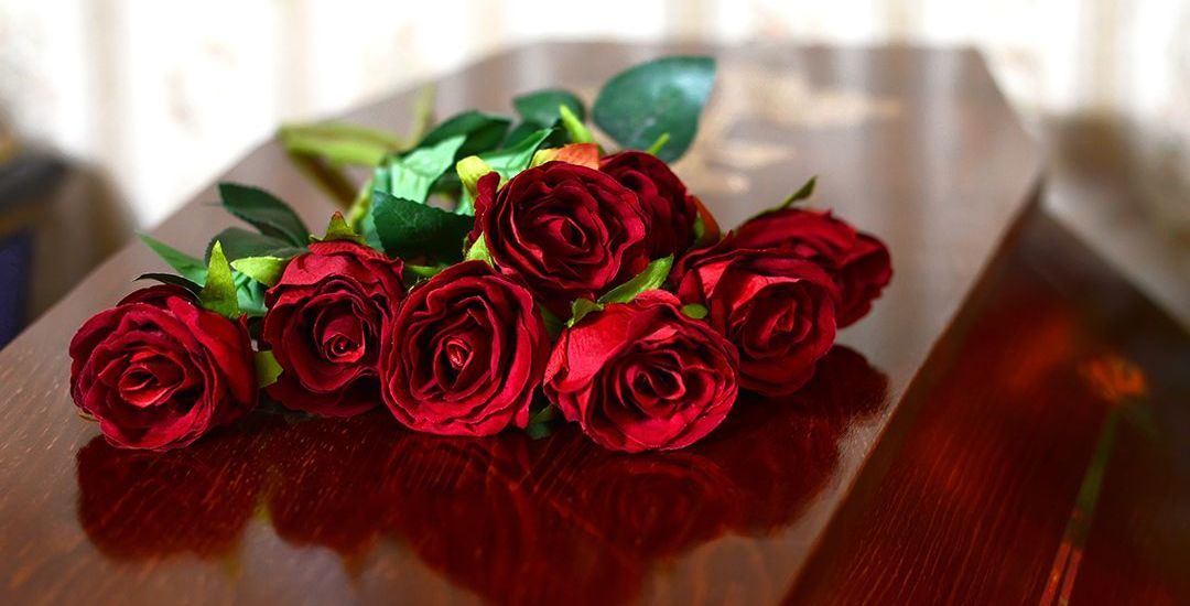 A bunch of red roses sitting on top of a wooden coffin.