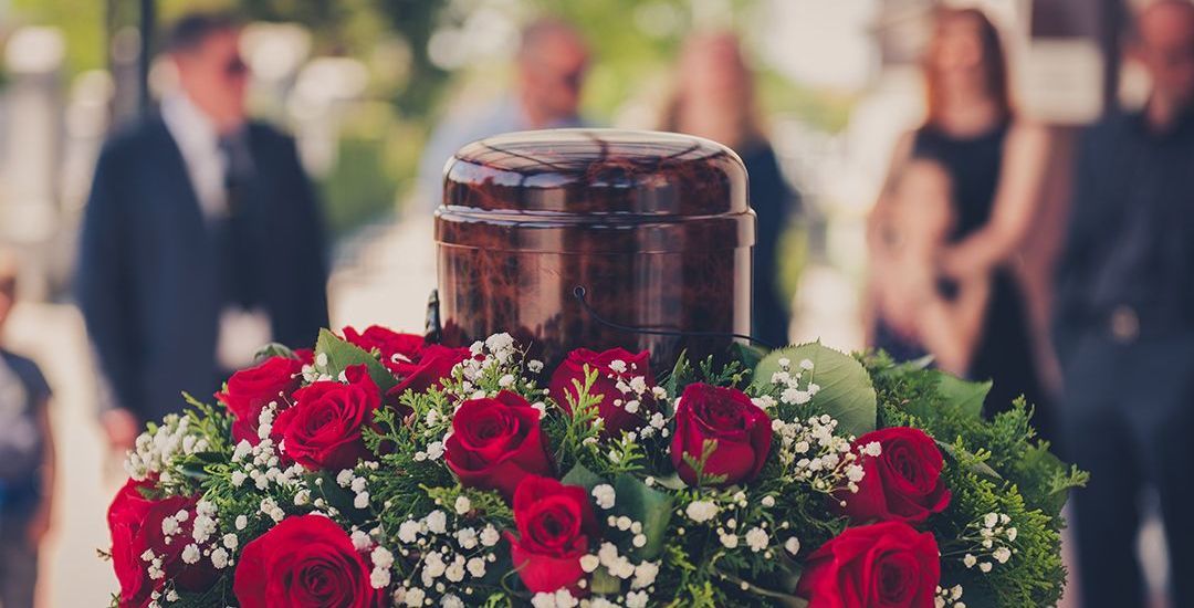 A urn surrounded by red roses and baby 's breath at a funeral.