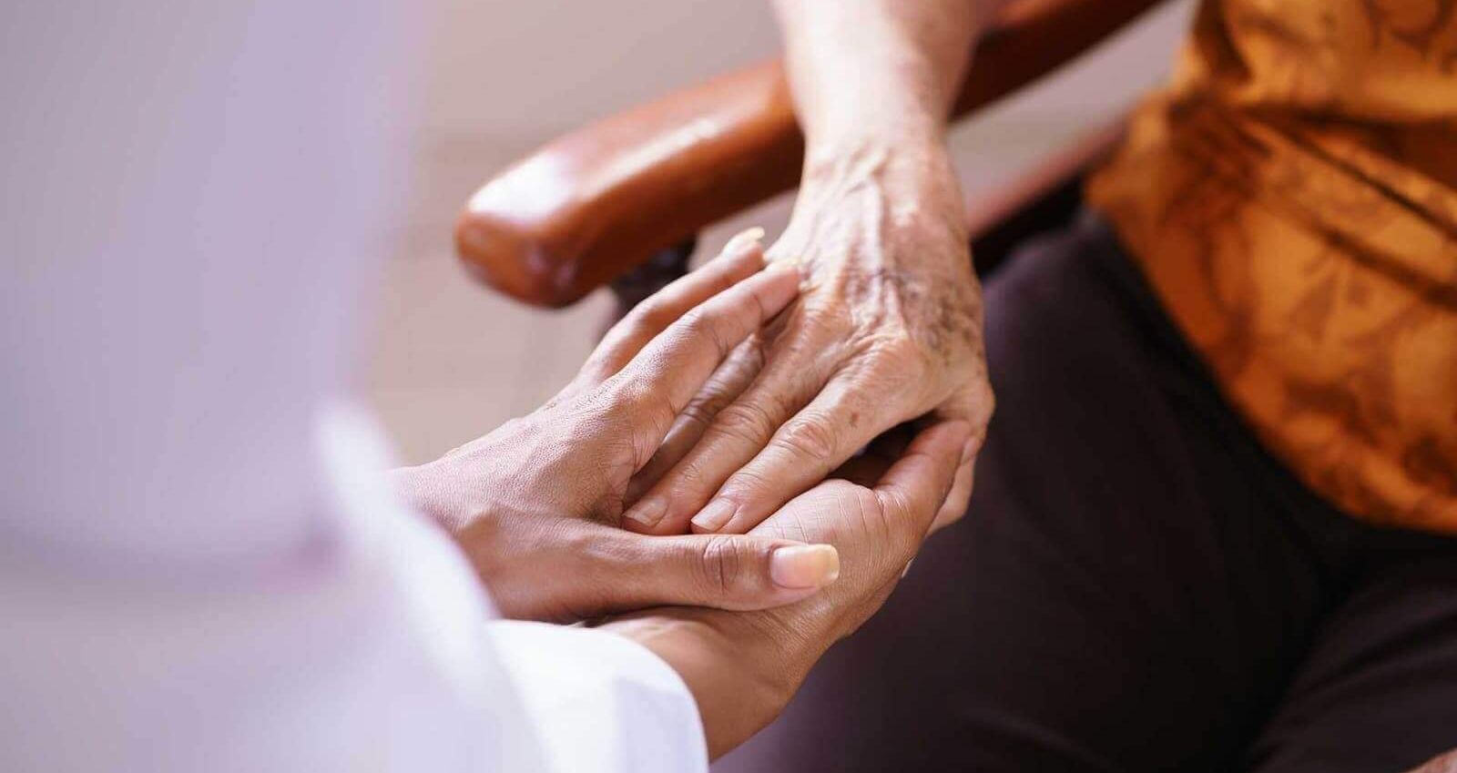 A person is holding another person 's hand while sitting in a chair.