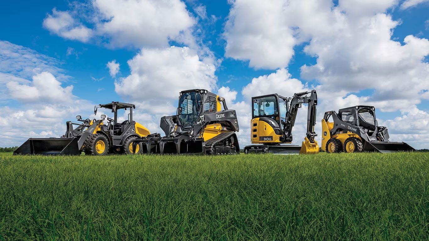 Construction vehicles on a green field under a blue sky with clouds.