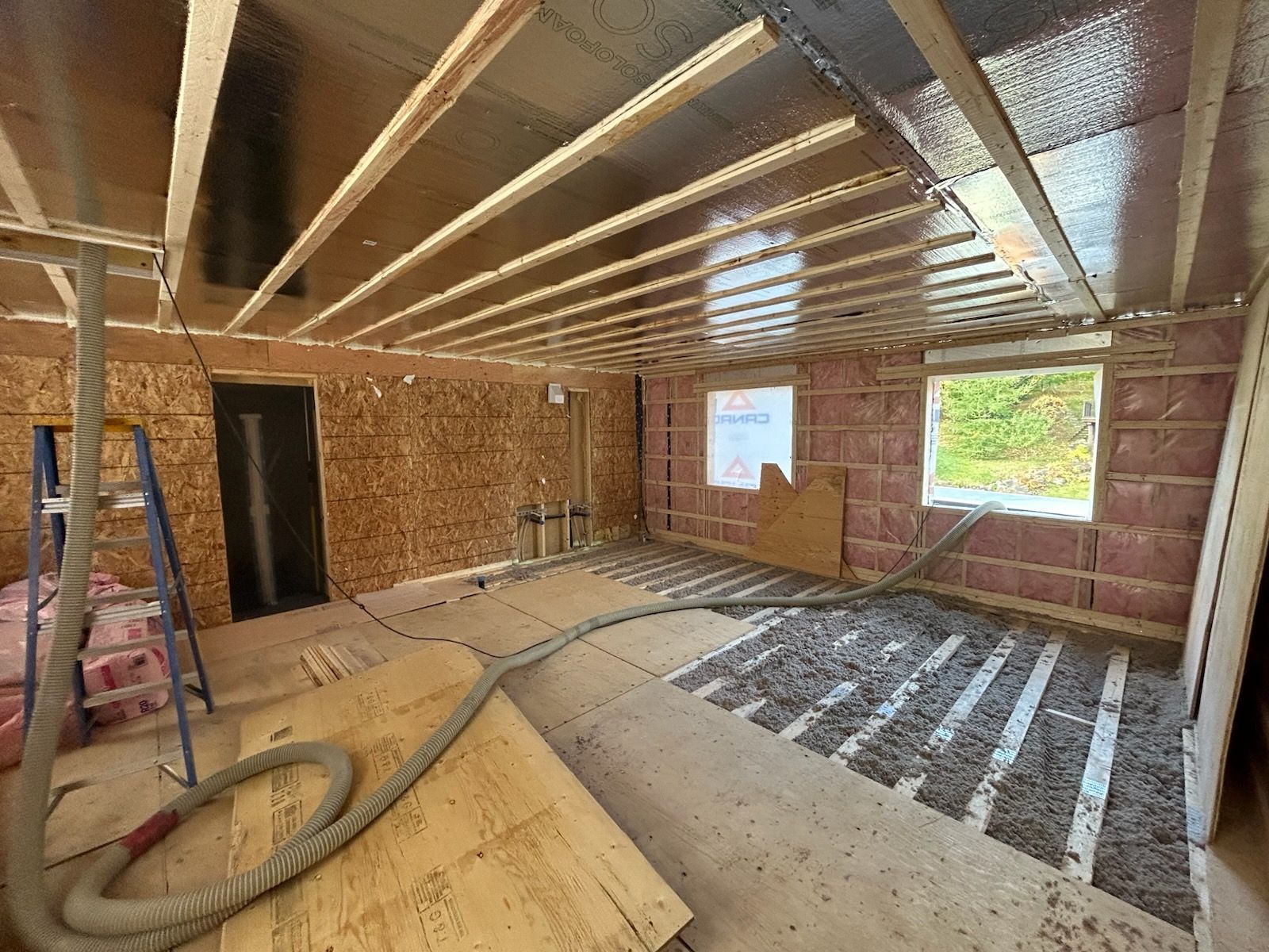 Intérieur en travaux : charpente apparente, isolation et murs non finis.