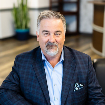 Man in a blue plaid blazer seated in an office, smiling at the camera