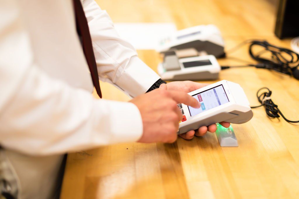 Person using a handheld payment terminal at a wooden table with cables and small devices nearby