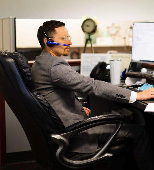 Man in a gray suit wearing a headset working at a desk in an office chair