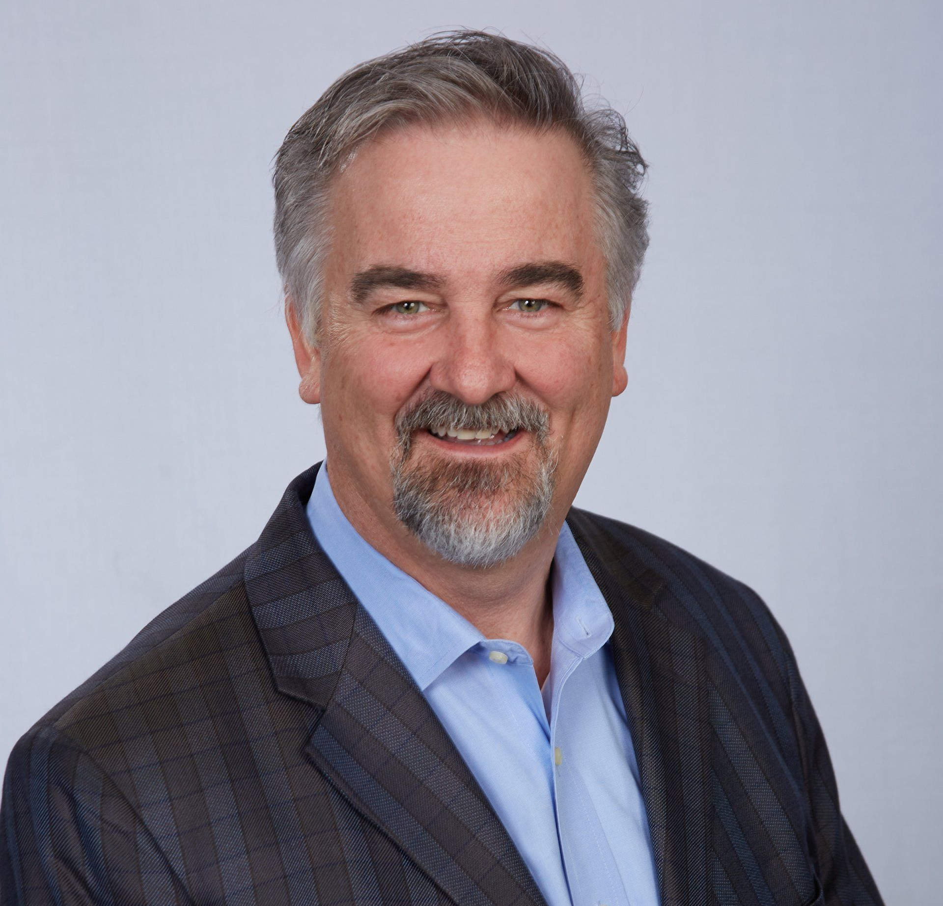 Portrait of a smiling man in a dark blazer and blue shirt against a light gray background