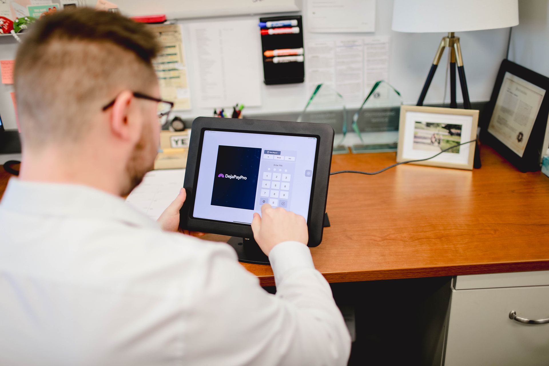 Person using a tablet at a desk in an office, viewing a dark screen with charts and controls.