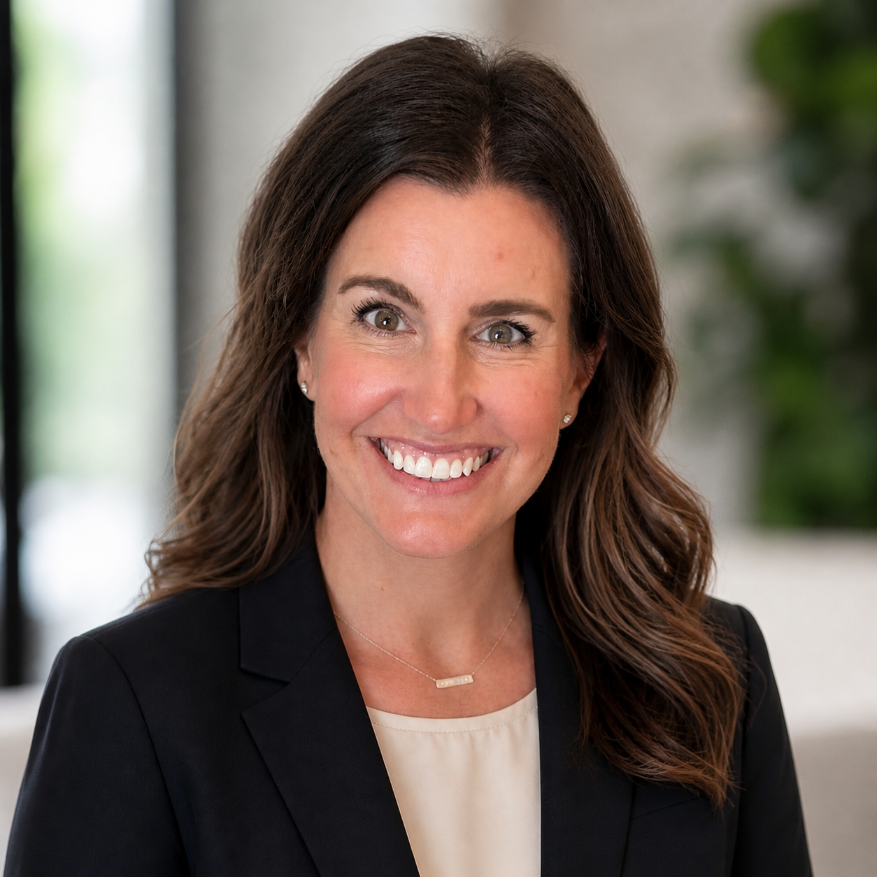 Portrait of a smiling woman in a black blazer against a bright, blurred background