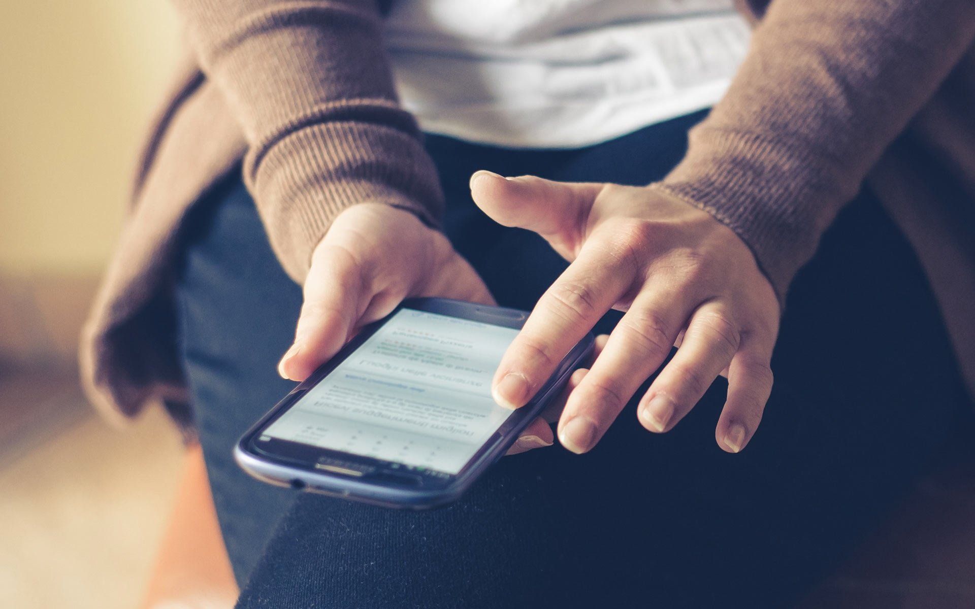 Hands typing on a smartphone while seated on a couch