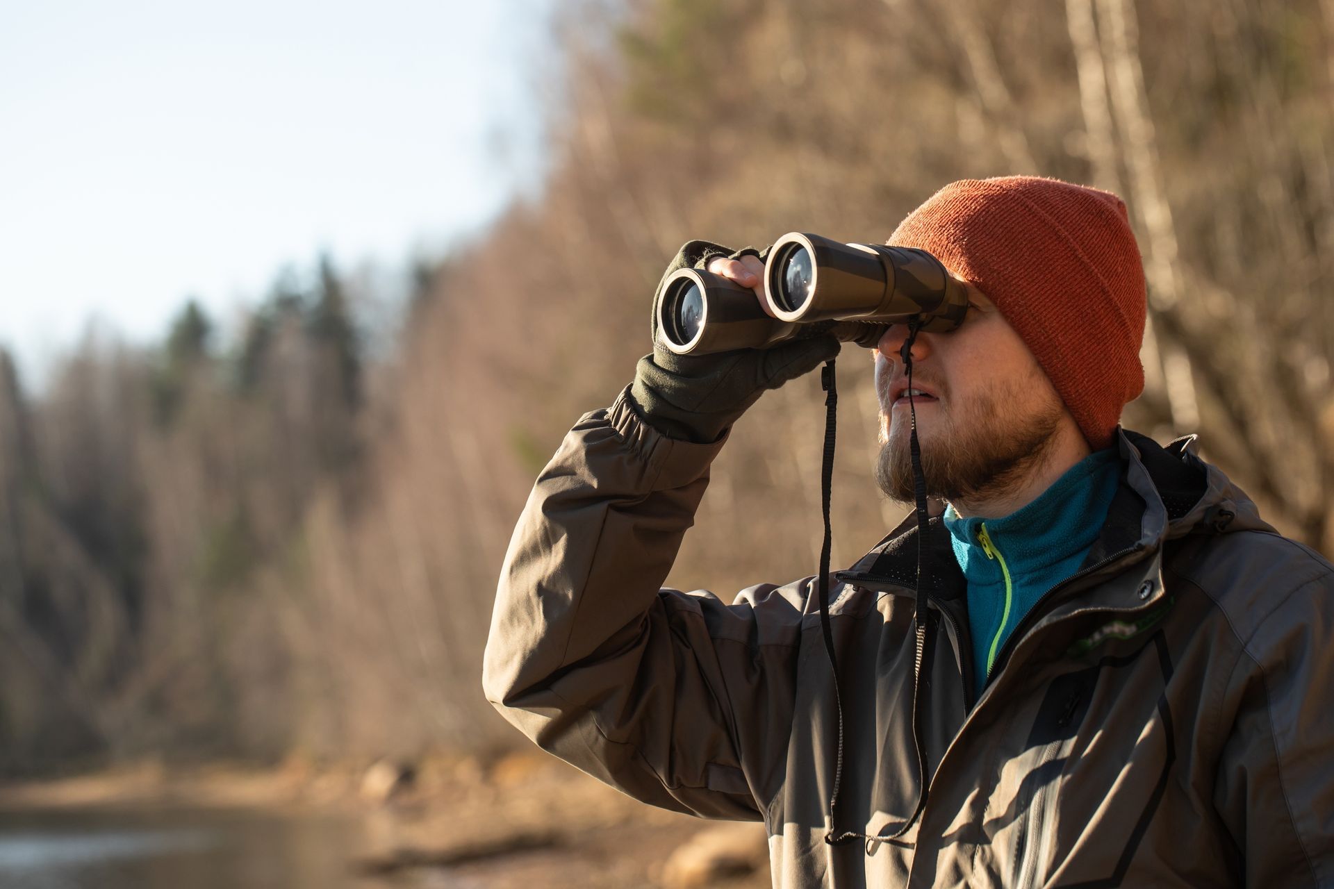 Person in an orange knit hat looking through binoculars in a wooded outdoor setting