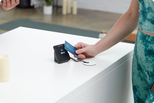 Person swipes a blue card on a white countertop payment terminal