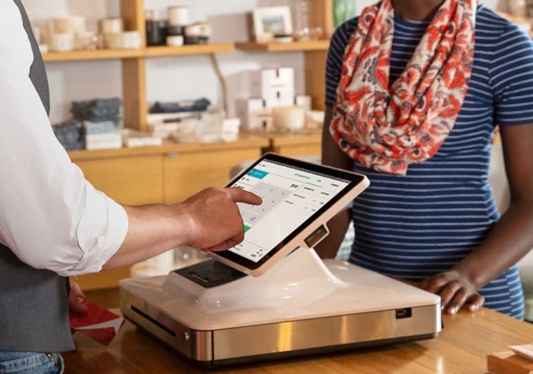 Customer tapping a digital payment terminal at a café counter