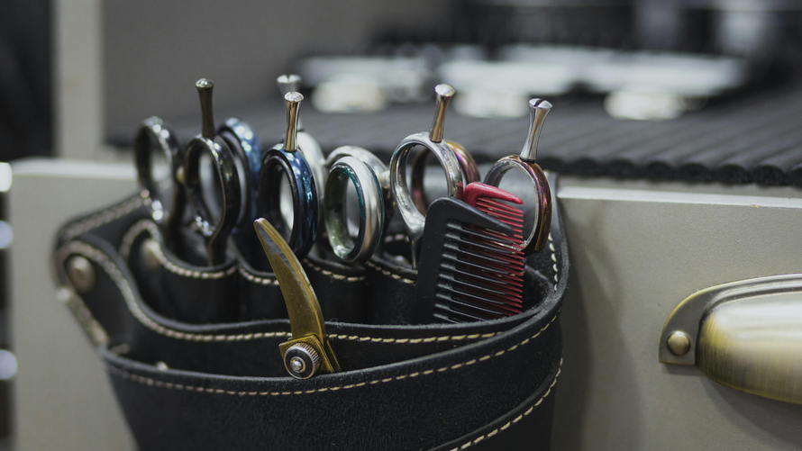 A black leather salon holster holding several pairs of shears and a red comb.