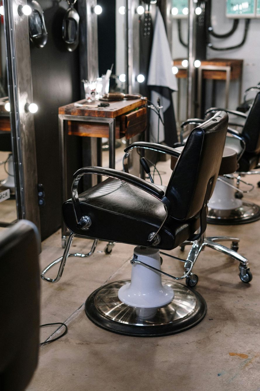 Black salon chairs in a studio with light-up mirrors and wooden work stations.