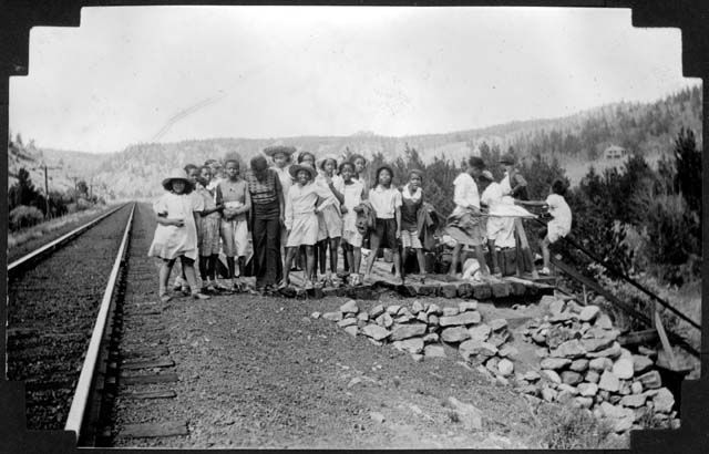 A black and white photo of a group of people standing on train tracks.