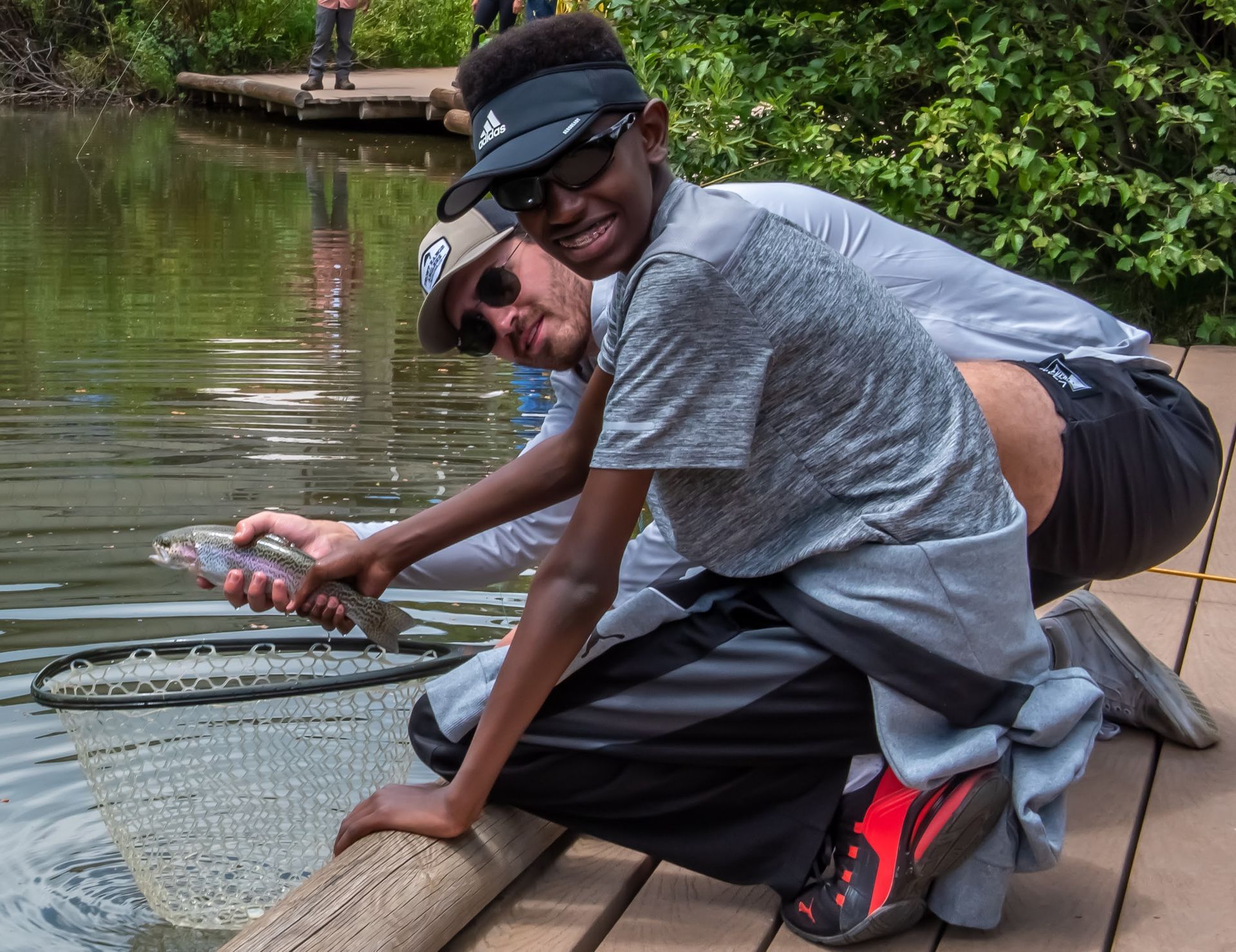 A man and a boy are kneeling next to a body of water.