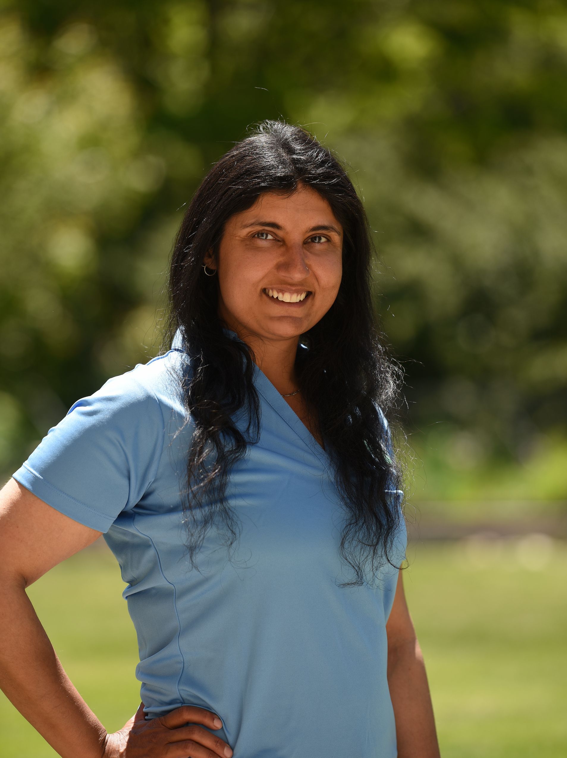 A woman in a blue shirt is standing with her hands on her hips.