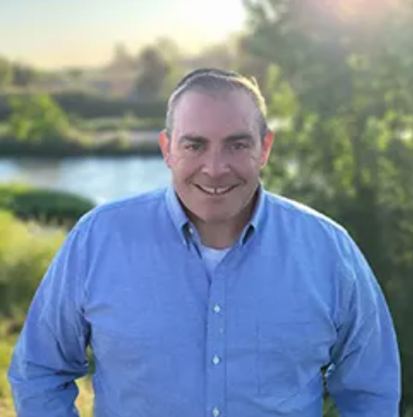 A man in a blue shirt is standing in front of a body of water.