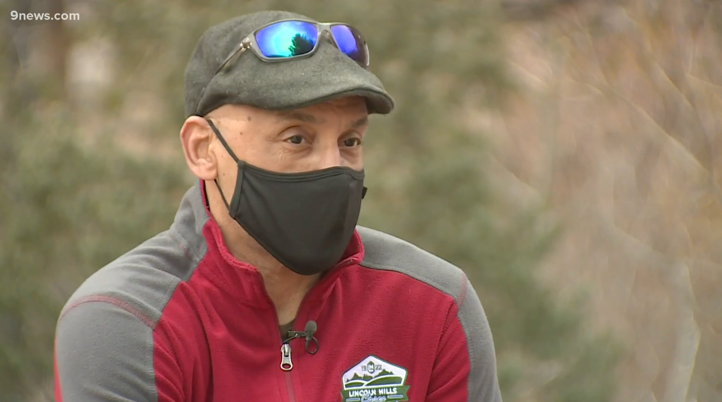 A man wearing a hat and sunglasses is wearing a face mask.
