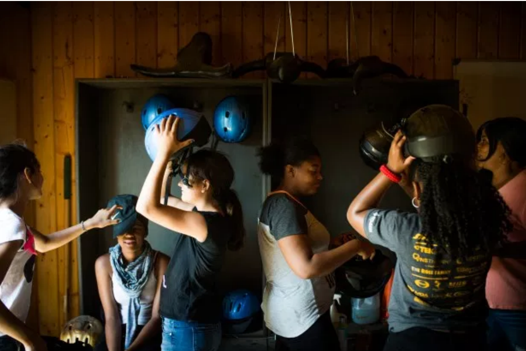A group of young women are playing with helmets in a room.