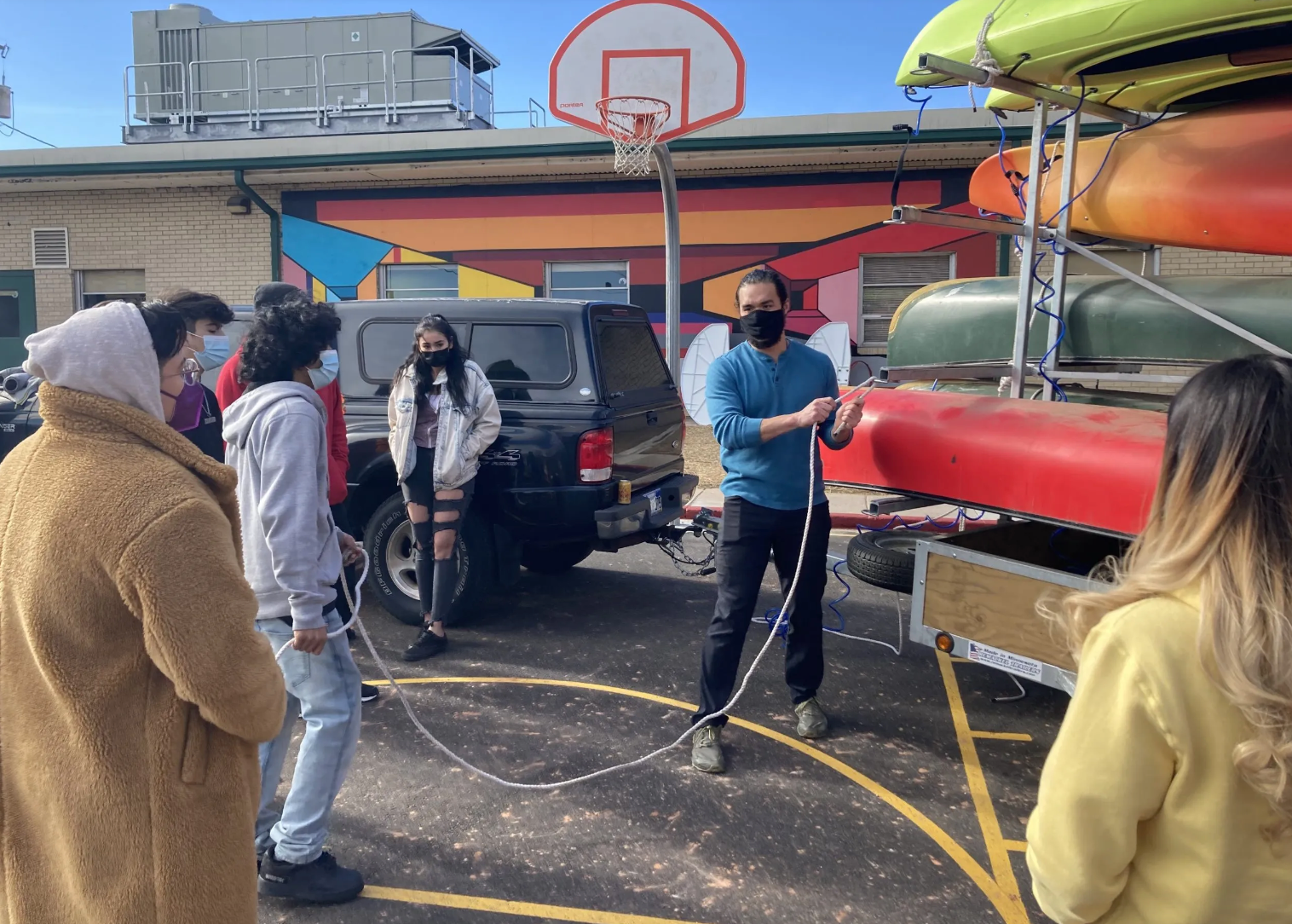 A man is teaching a group of people how to tie a canoe to a trailer.