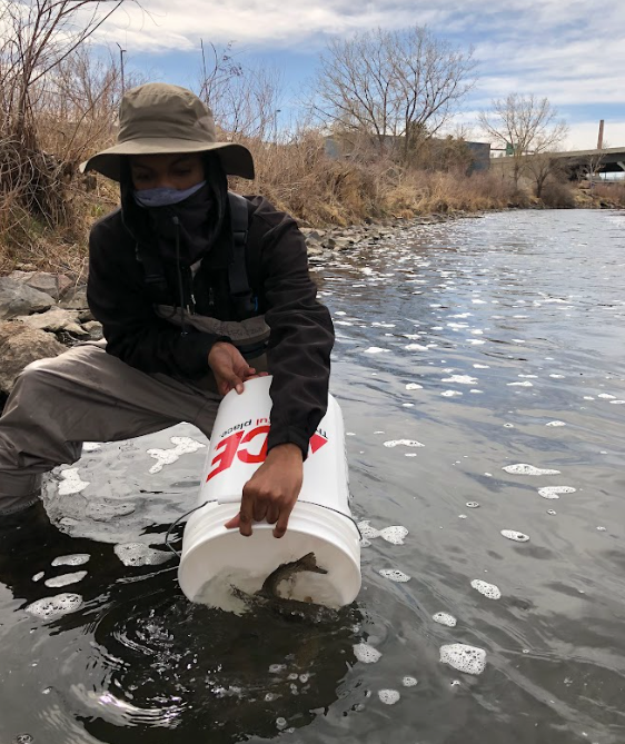 A man in a hat is kneeling in the water holding a bucket that says coca cola on it
