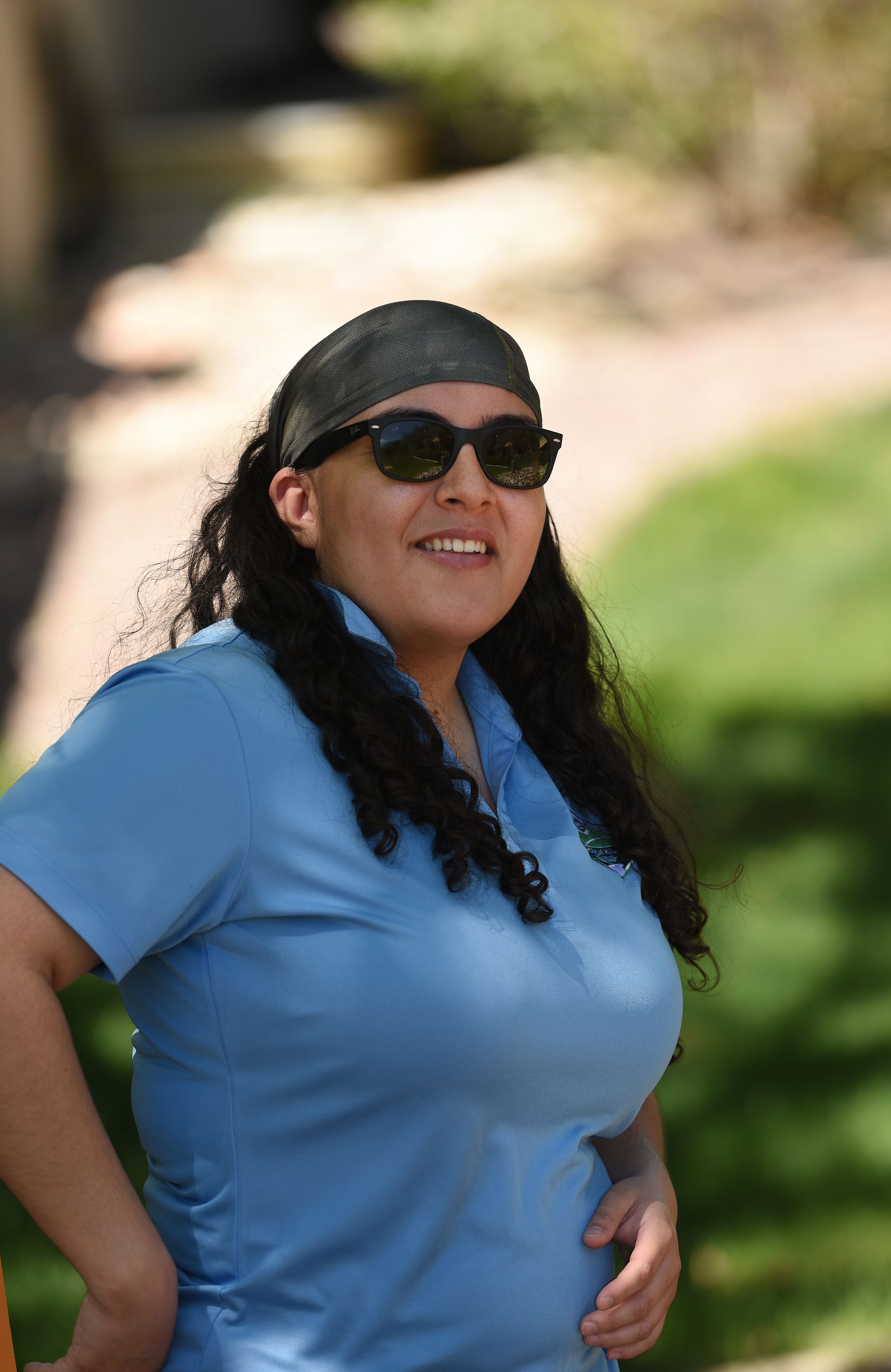 A woman wearing sunglasses and a bandana is standing in a park.