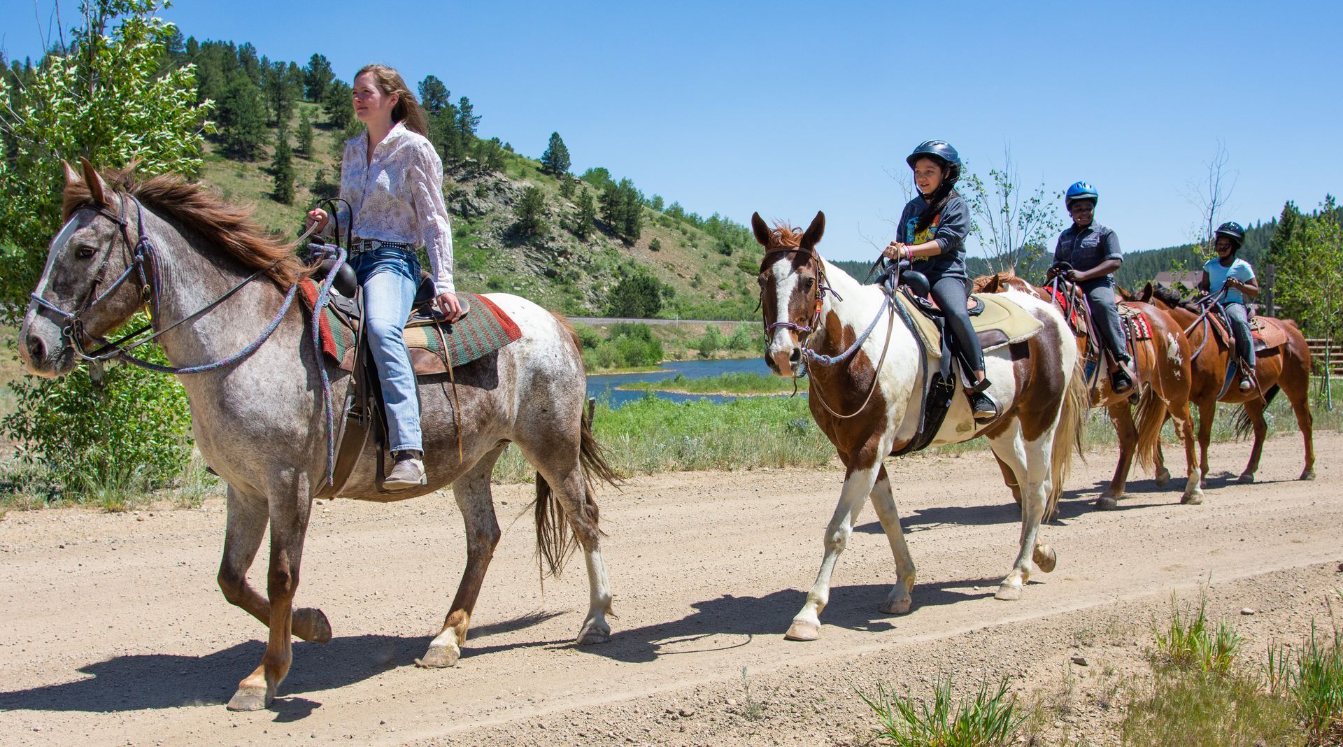 A group of people riding horses down a dirt road