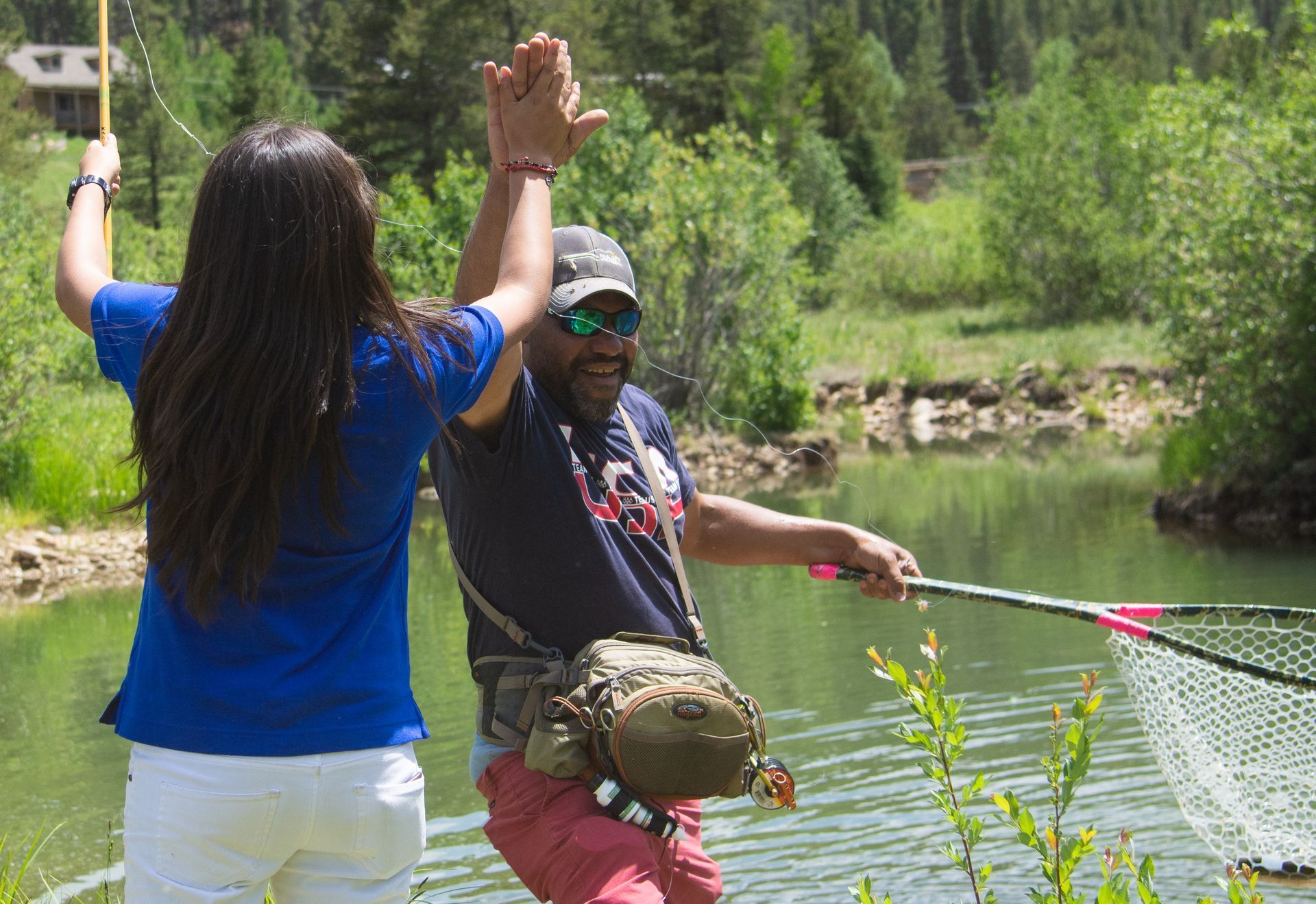 A man and a woman are fishing in a lake and giving each other a high five.